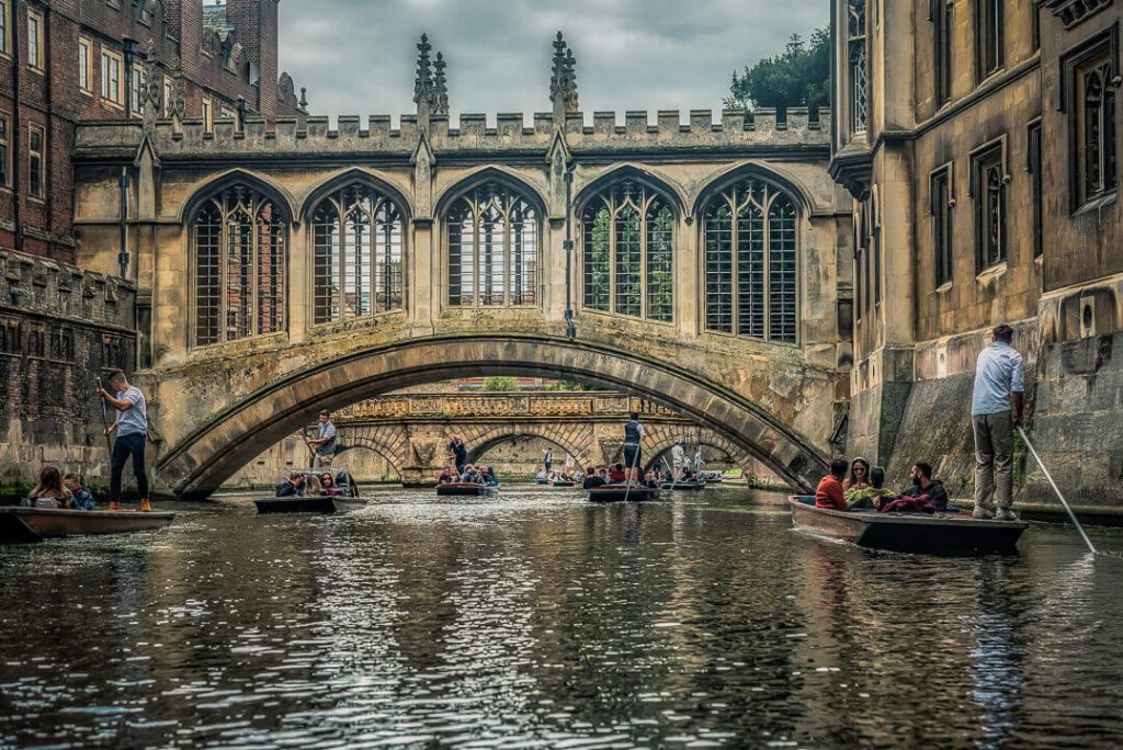 An image showing the Bridge of Sighs along River Cam in Cambridge, Cambridgeshire. Several punting boats are on the river with tourists on board.